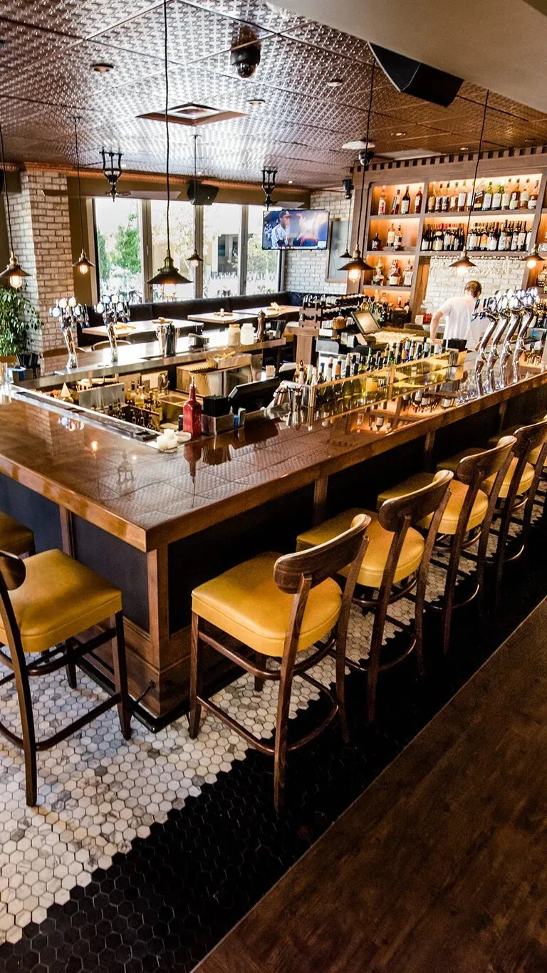 The Terza bar, taps and bottles behind it and tan leather stools along the counter