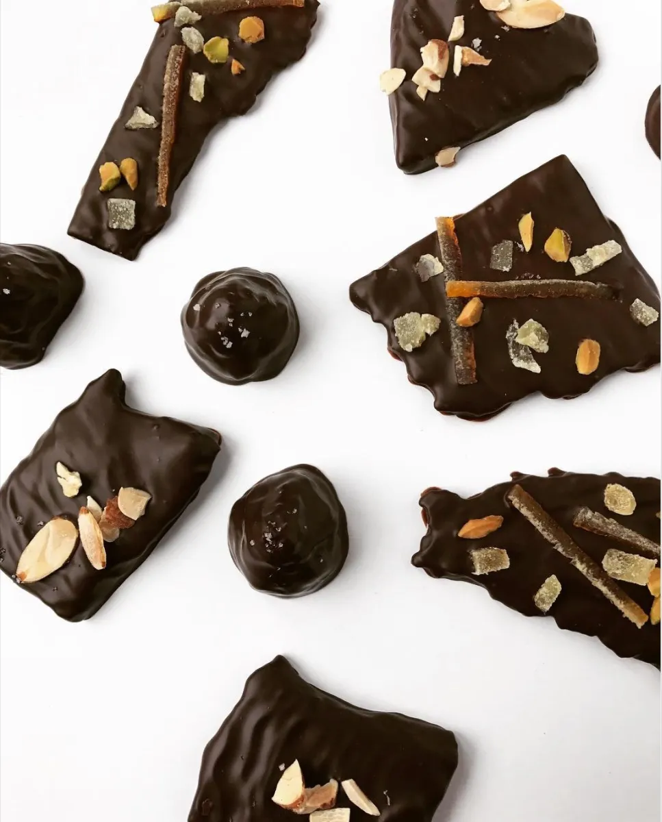 Dark chocolate bark and bonbons scattered on white, from above