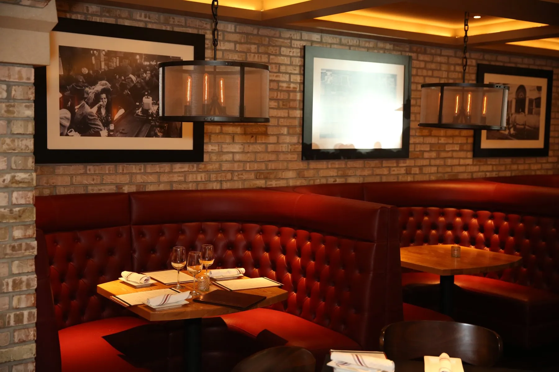 A red tufted banquette under framed prints and pendant lights