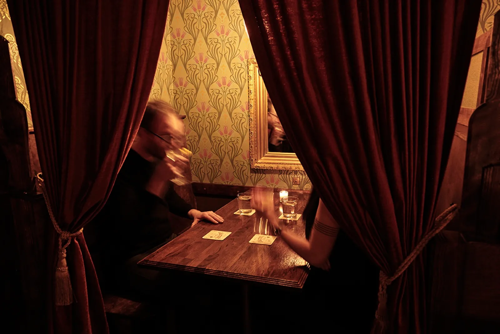 A curtained booth at Volstead’s, two guests at a table against patterned wallpaper and a gilt mirror