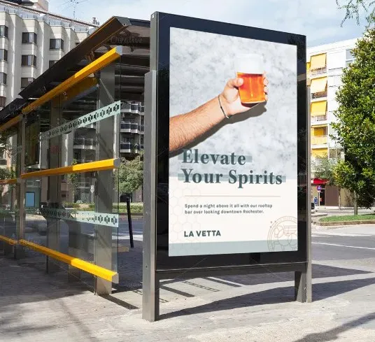 An “Elevate Your Spirits” poster lit in a downtown Rochester bus shelter
