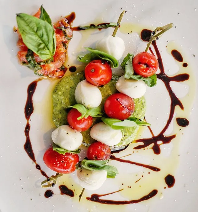 A caprese of tomato, mozzarella and basil, dressed with balsamic