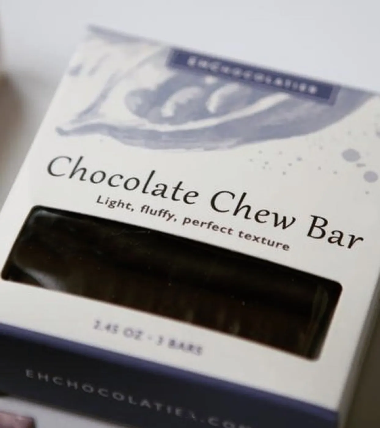 The Chocolate Chew Bar box, the dark bar showing through its window under lilac brushwork