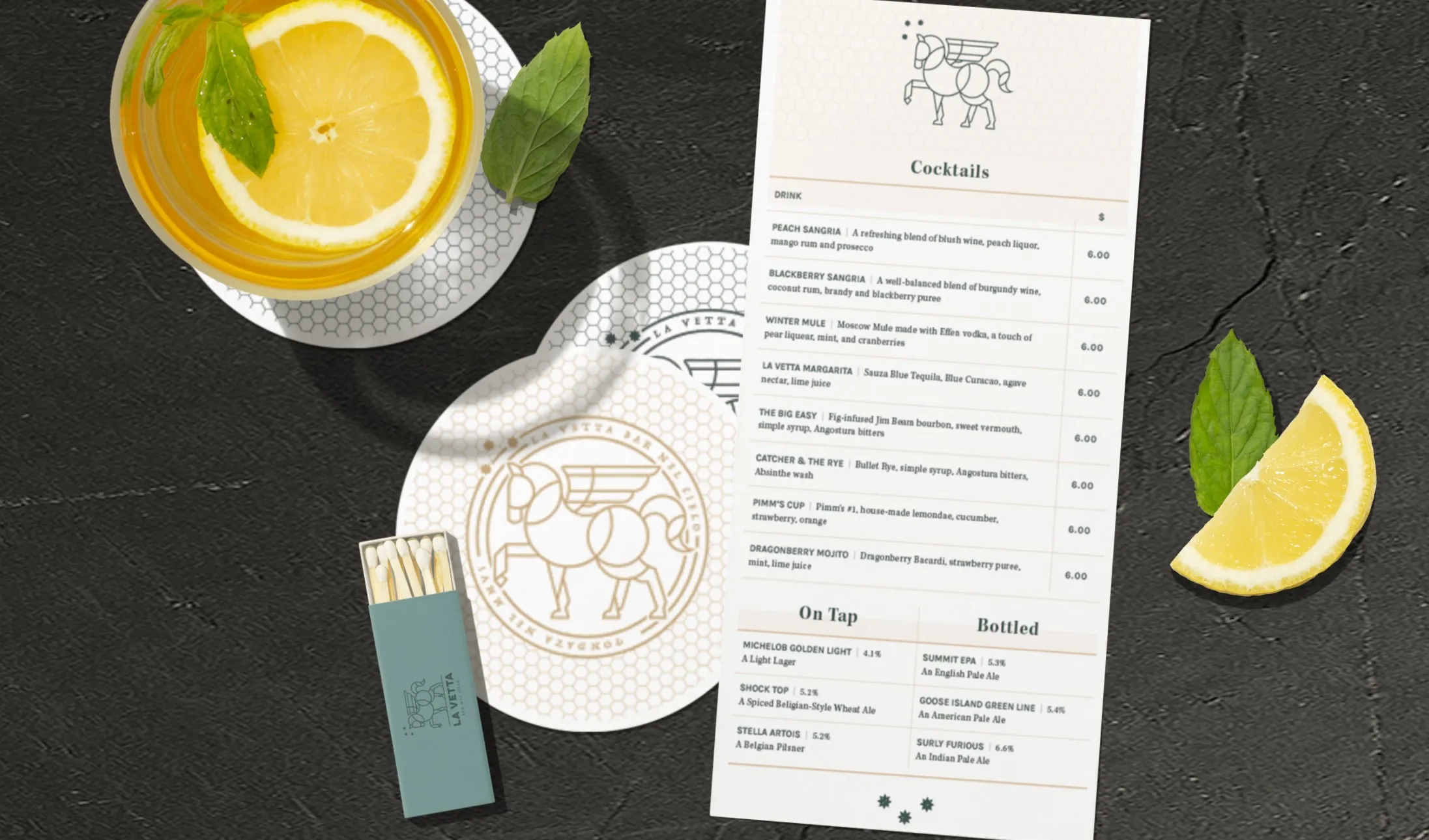 The La Vetta cocktail menu on slate with a branded coaster, a matchbox and a cut lemon