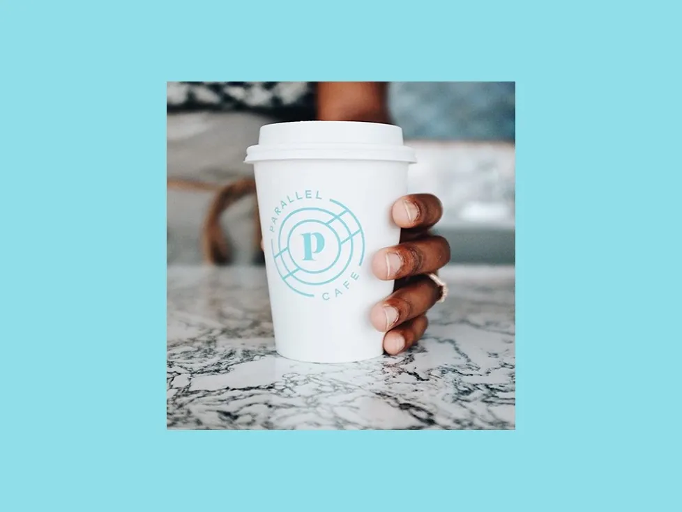 A hand setting down a Parallel cup on marble, framed on an aqua panel