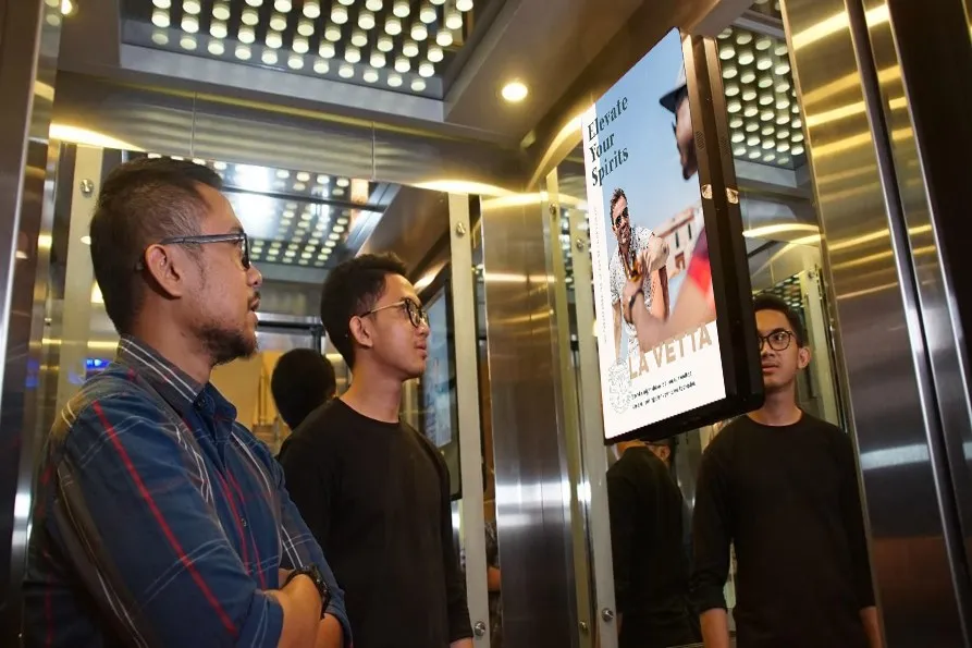 Guests riding the H3 Plaza elevator beside a lit La Vetta “Elevate Your Spirits” panel