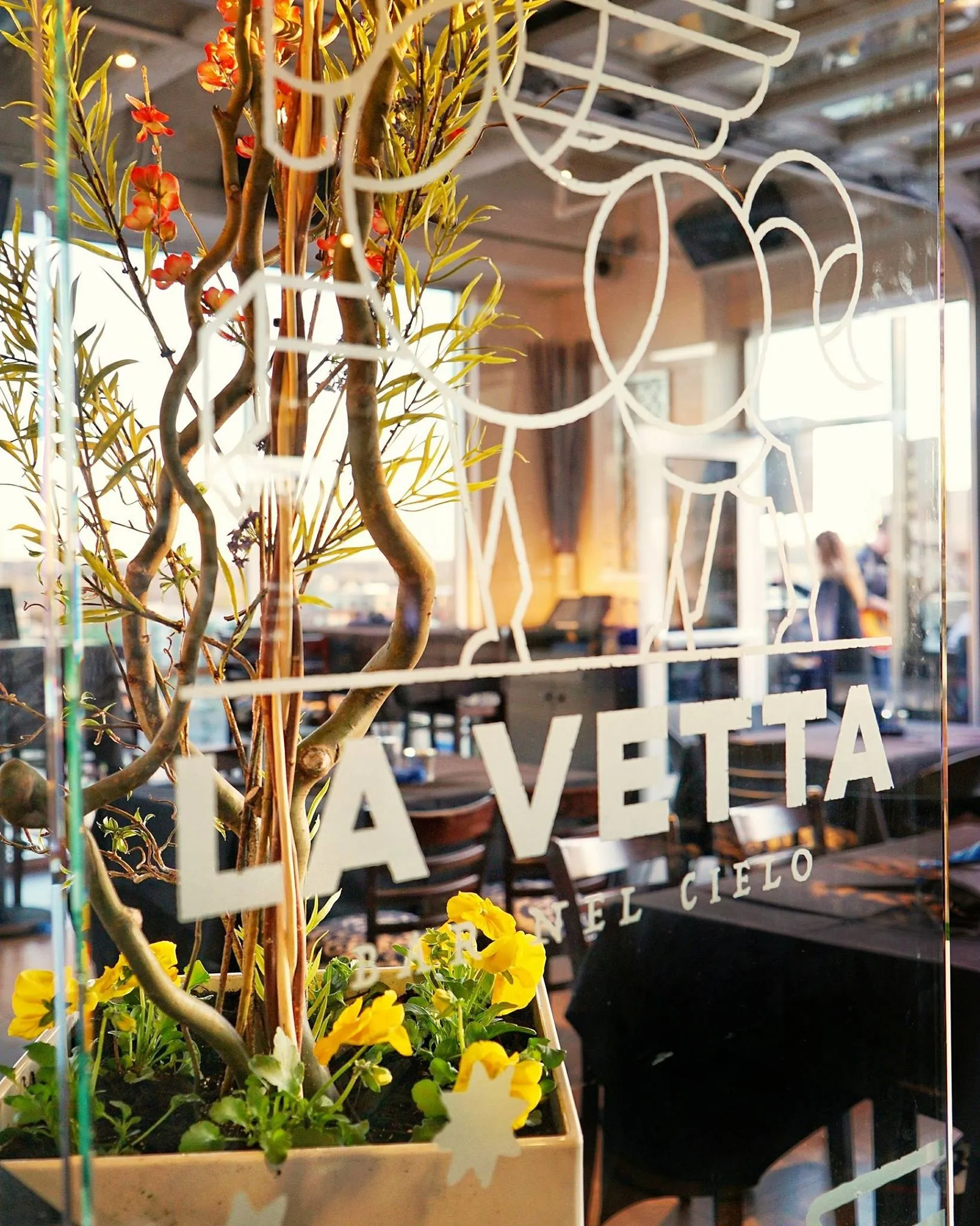 The La Vetta lettering across the rooftop's glass wall, planters and string lights in front of it