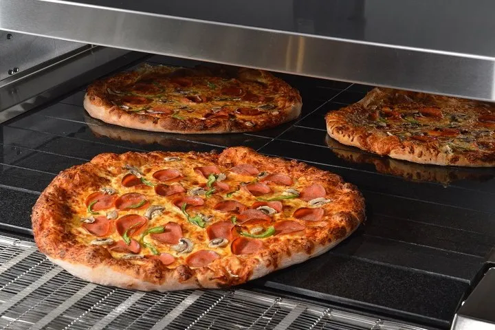 Pizzas moving across the heated stone slabs of the Hot Rocks conveyor oven