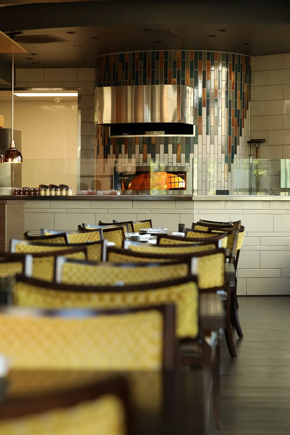 Rows of yellow-backed chairs in the Hazelwood dining room, facing the open kitchen and its tiled wood-fired oven