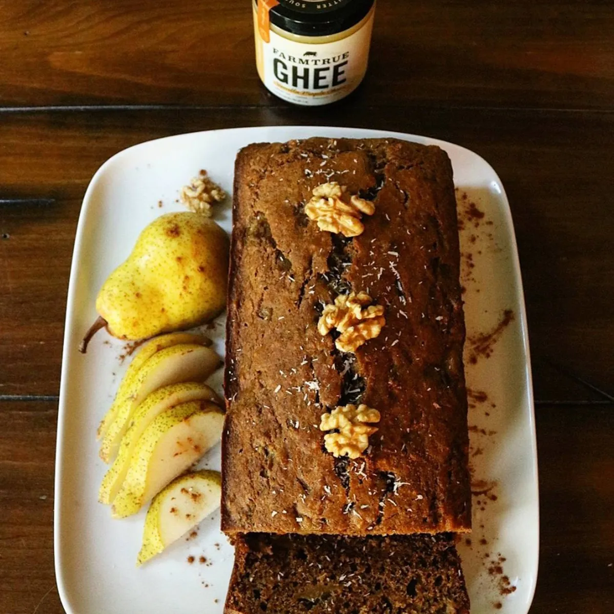 A slice of banana bread with pear and walnuts, a jar of ghee behind