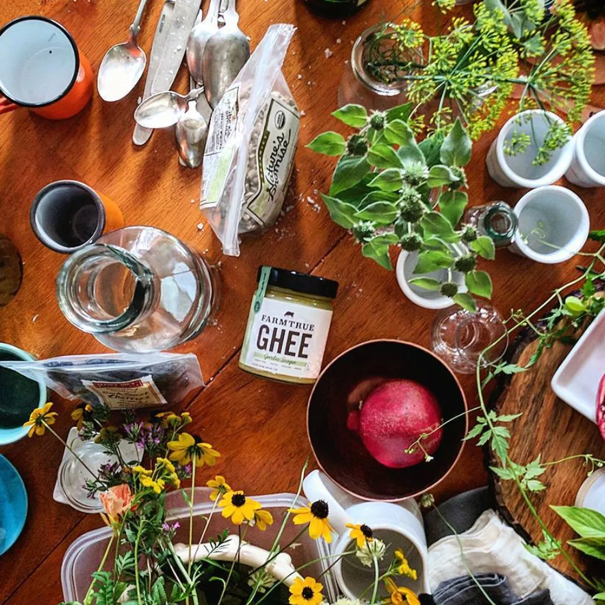 A table laid with herbs, flowers, jars and a FarmTrue ghee, from above