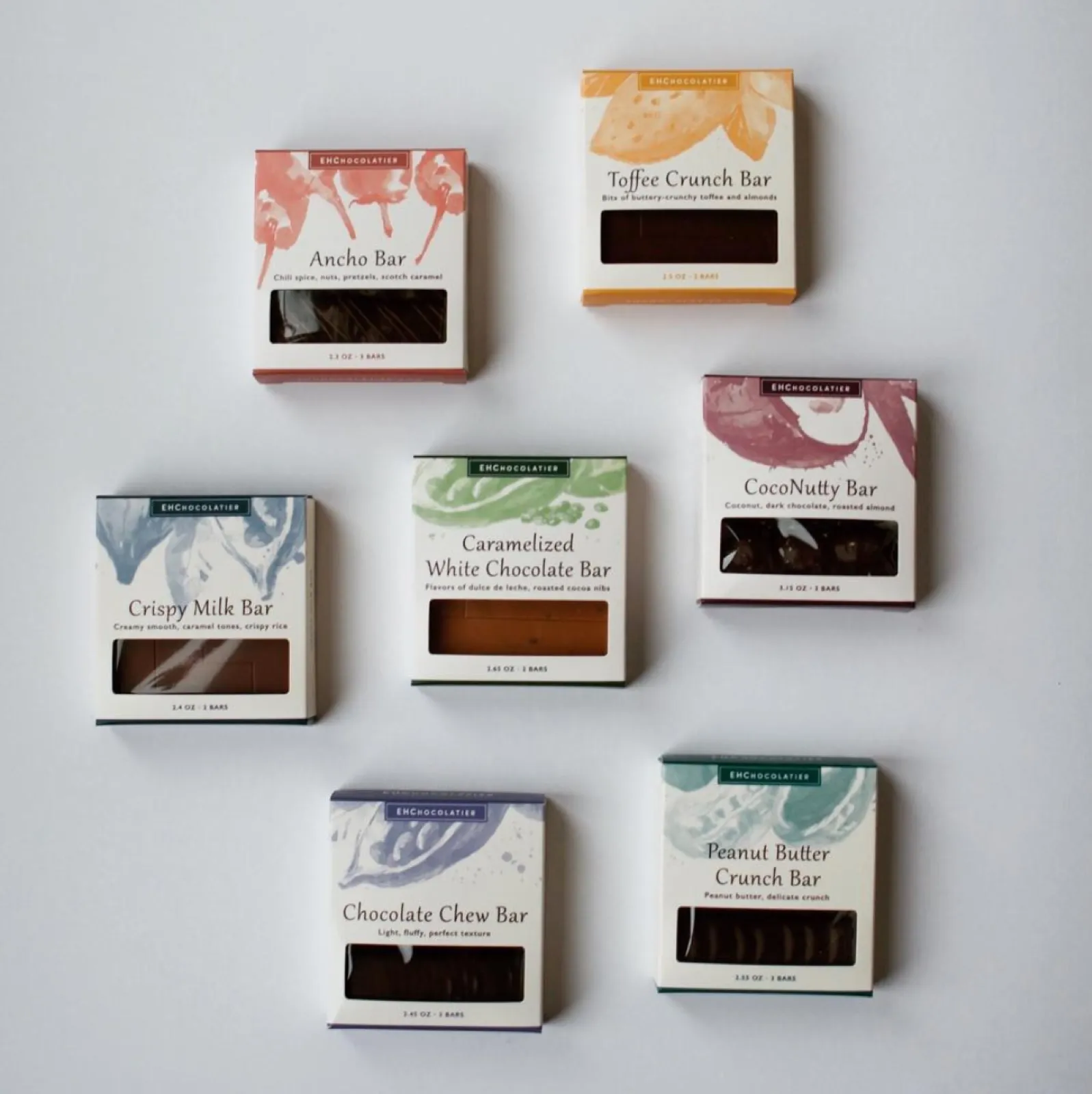 The complete EH Chocolatier lineup: seven cream boxes, each with its own painterly color and a window onto the bar inside