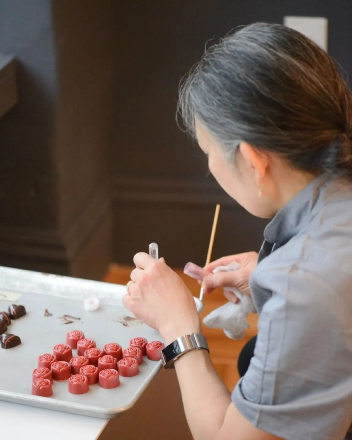 A chocolatier at the bench, piping a tray of bonbons by hand
