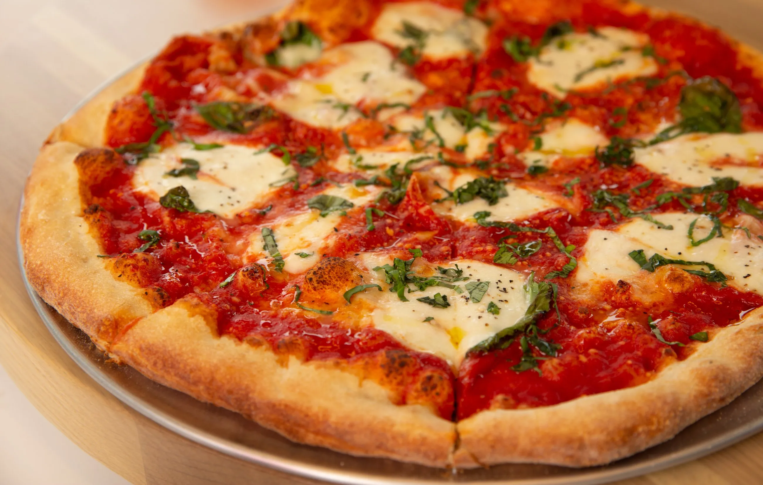 A Pizza Novara margherita on a steel tray, fresh mozzarella and basil over a blistered stone-baked crust