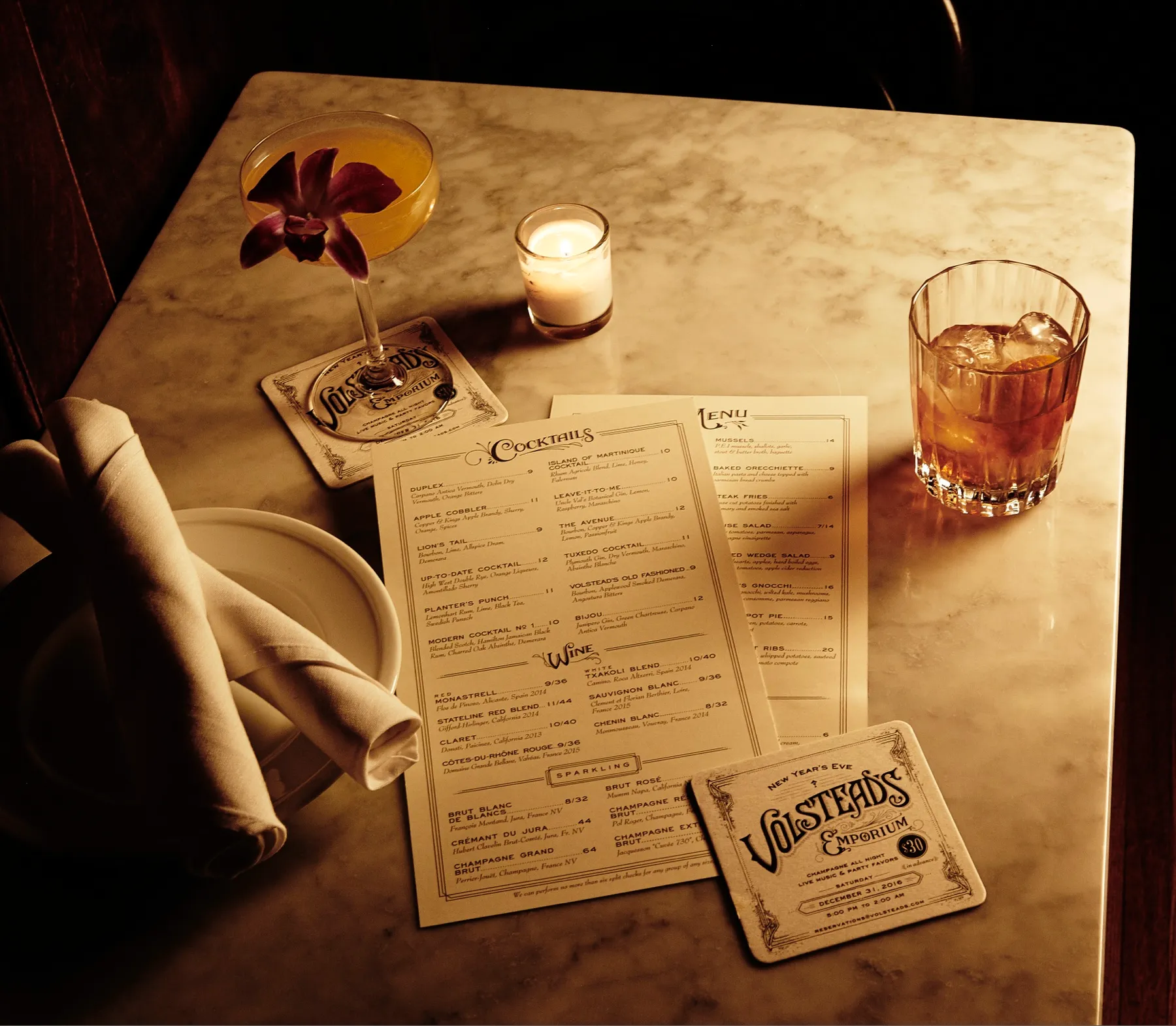 A marble table at Volstead’s with the cocktail and food menus, a coaster, a coupe and an old fashioned