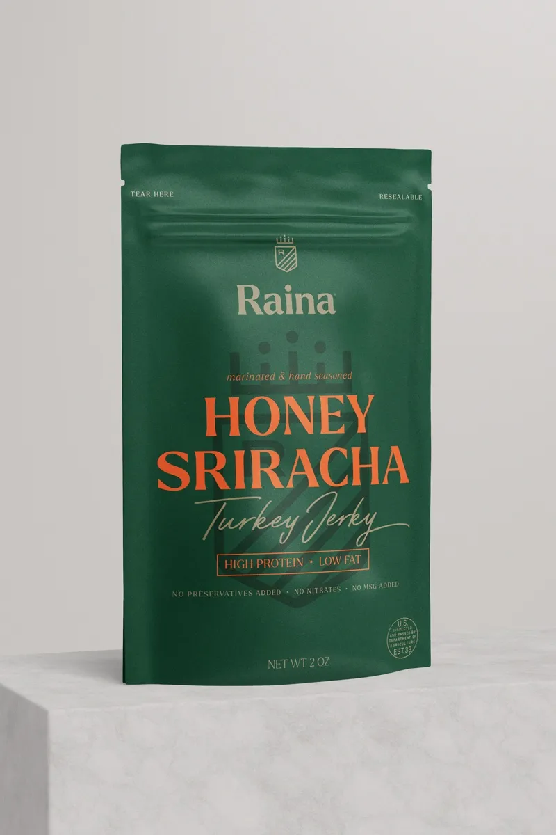 Raina Honey Sriracha turkey jerky in its green pouch, on a stone plinth