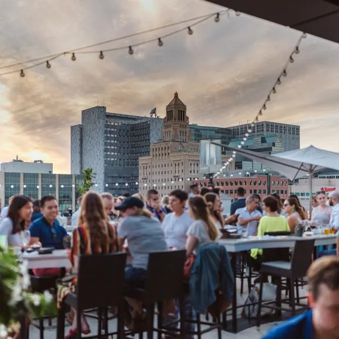 Guests filling the La Vetta rooftop at dusk under string lights, the Rochester skyline behind