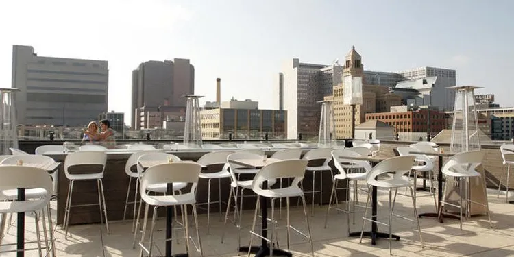 The La Vetta rooftop by day, bar-height tables and stools set out along the parapet against the downtown Rochester skyline