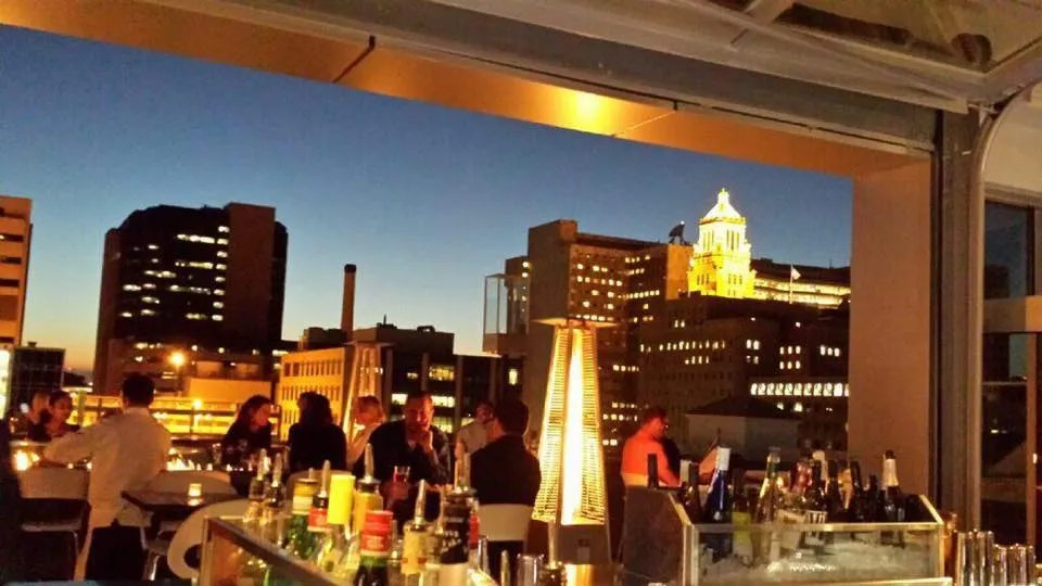 The La Vetta rooftop at dusk: guests at tables along the parapet, heat lamps lit and the downtown Rochester skyline behind