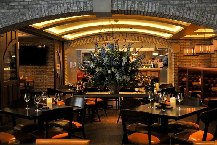 The Terza dining room, tables set beneath a vaulted ceiling with a tall floral arrangement at the centre