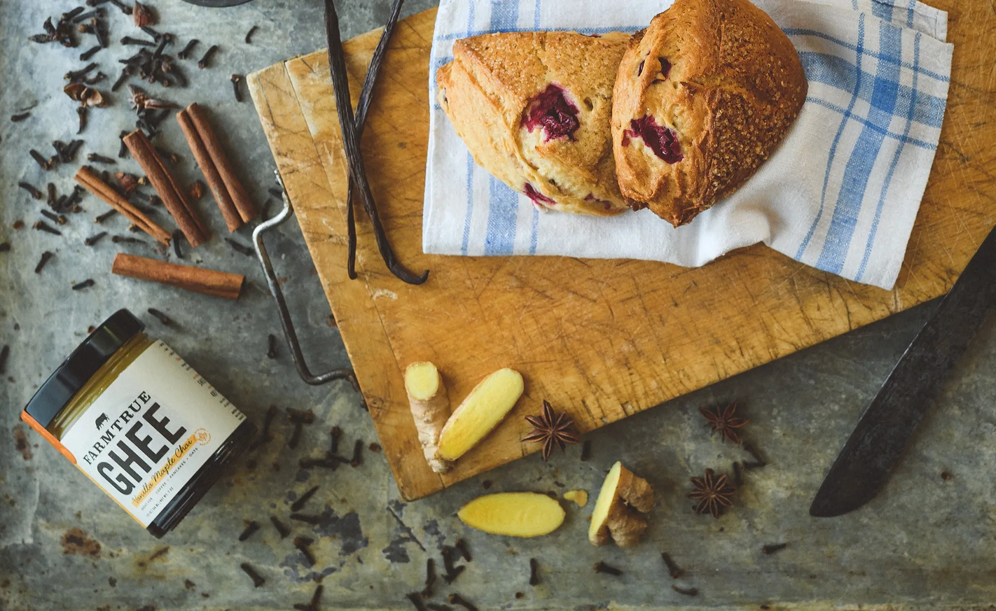 A jar of FarmTrue ghee on a board with scones, cinnamon sticks and a knife