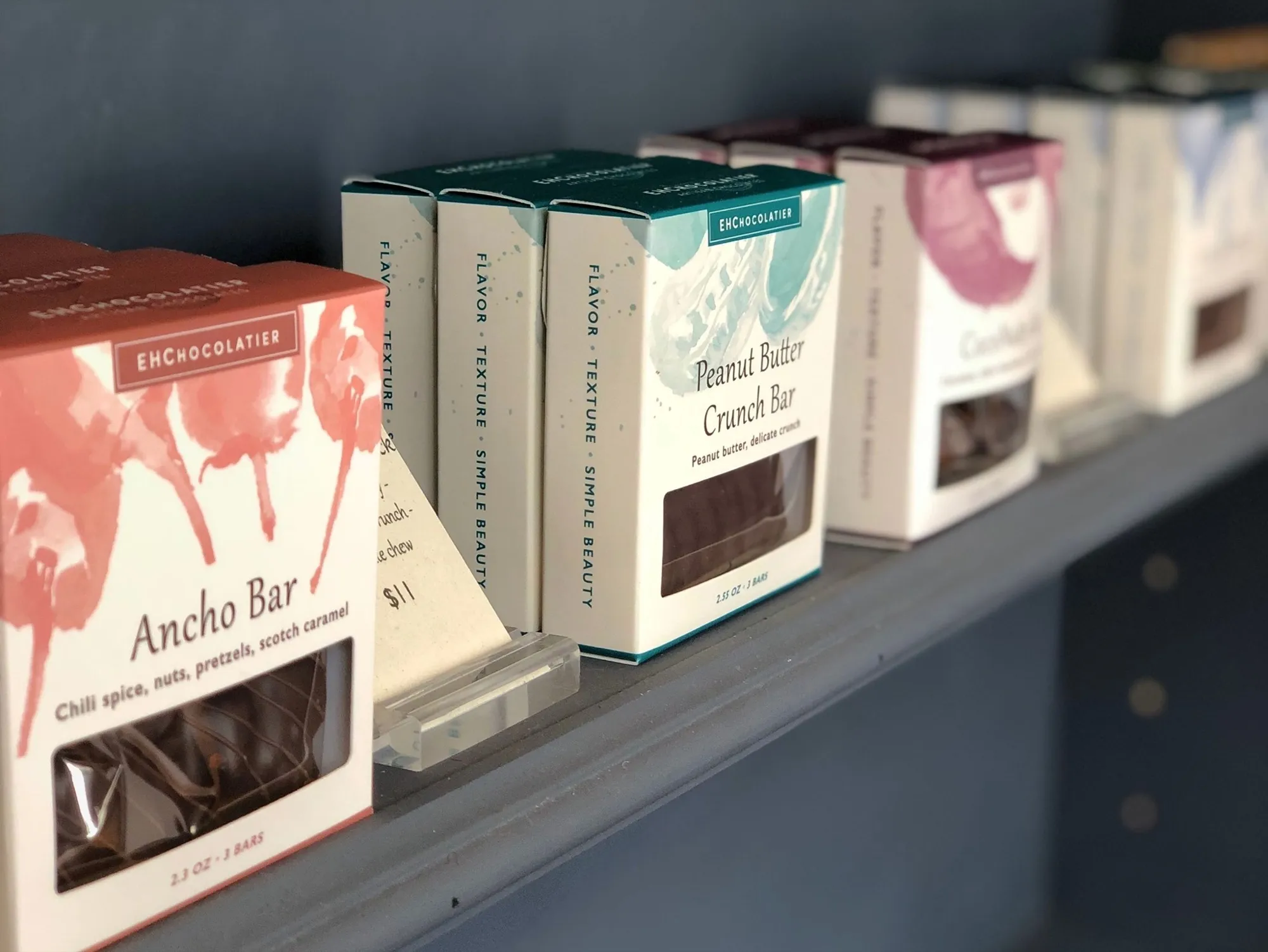 EH Chocolatier boxes lined up on a shop shelf, the painterly fronts facing out