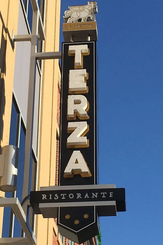 The Terza Ristorante blade sign against a clear sky, the lettering stacked down a black panel