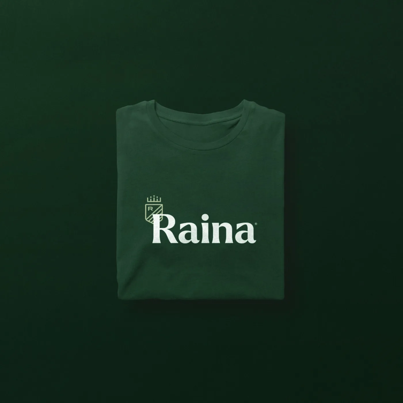 A folded green tee with the Raina crest and wordmark